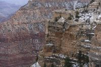 a rocky cliff covered in snow in the mountains near an area with trees and cliffs