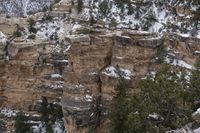 a rocky cliff covered in snow in the mountains near an area with trees and cliffs