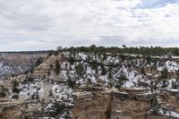 a rocky cliff covered in snow in the mountains near an area with trees and cliffs