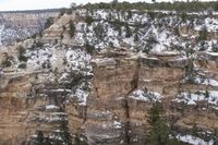 a rocky cliff covered in snow in the mountains near an area with trees and cliffs