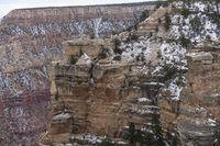 a rocky cliff covered in snow in the mountains near an area with trees and cliffs