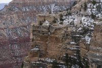 a rocky cliff covered in snow in the mountains near an area with trees and cliffs