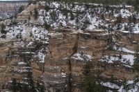 a rocky cliff covered in snow in the mountains near an area with trees and cliffs