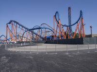 several orange and blue roller coasters in an amusement park lot during the day with no clouds