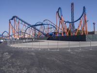 several orange and blue roller coasters in an amusement park lot during the day with no clouds