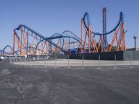 several orange and blue roller coasters in an amusement park lot during the day with no clouds