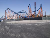 several orange and blue roller coasters in an amusement park lot during the day with no clouds