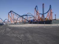 several orange and blue roller coasters in an amusement park lot during the day with no clouds