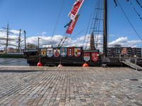 the ship has banners on it near a dock with boats in the water and buildings