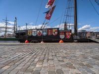 the ship has banners on it near a dock with boats in the water and buildings