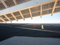 a parking lot filled with lots of empty asphalt under a roof near a beach with lots of sun shining through the roof