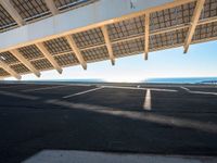 a parking lot filled with lots of empty asphalt under a roof near a beach with lots of sun shining through the roof