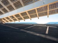 a parking lot filled with lots of empty asphalt under a roof near a beach with lots of sun shining through the roof