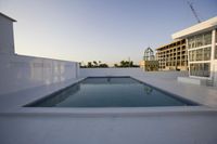 an empty swimming pool on the roof of a building at dusk with a crane in the background