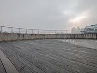 a view looking out from a rooftop deck in the fog with a wooden fence on top and buildings on the far side