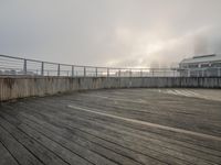 a view looking out from a rooftop deck in the fog with a wooden fence on top and buildings on the far side