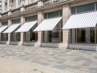 a row of windows that are covered with awnings on a sidewalk in front of a building