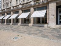 a row of windows that are covered with awnings on a sidewalk in front of a building