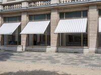 a row of windows that are covered with awnings on a sidewalk in front of a building