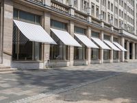 a row of windows that are covered with awnings on a sidewalk in front of a building