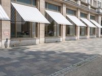 a row of windows that are covered with awnings on a sidewalk in front of a building