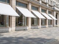 a row of windows that are covered with awnings on a sidewalk in front of a building