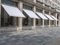 a row of windows that are covered with awnings on a sidewalk in front of a building