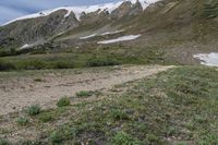 a person with a backpack walking down a rocky path in the mountains above snow capped mountains