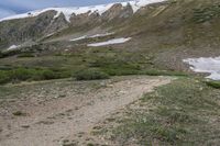 a person with a backpack walking down a rocky path in the mountains above snow capped mountains