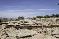 a rocky landscape with green shrubs and trees below it, and sky above the canyon