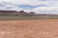 the desert has some dirt on it and mountains in the background under a cloudy blue sky