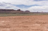 the desert has some dirt on it and mountains in the background under a cloudy blue sky