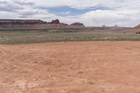 the desert has some dirt on it and mountains in the background under a cloudy blue sky