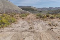 the dirt road is dirted down in a canyon of mountains and shrubs, dirt trails, and dry grass