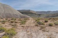 the dirt road is dirted down in a canyon of mountains and shrubs, dirt trails, and dry grass