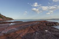 a rock shoreline with a view of the ocean at sunset, with clouds overhead and rocks in foreground