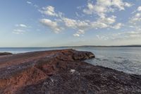 a rock shoreline with a view of the ocean at sunset, with clouds overhead and rocks in foreground