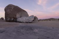 a large rock sitting on top of a field near a dry landscape under a pink sky