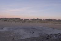 a large rock sitting on top of a field near a dry landscape under a pink sky