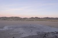 a large rock sitting on top of a field near a dry landscape under a pink sky