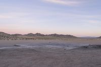 a large rock sitting on top of a field near a dry landscape under a pink sky