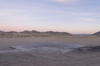 a large rock sitting on top of a field near a dry landscape under a pink sky