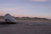 a large rock sitting on top of a field near a dry landscape under a pink sky