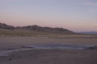 a large rock sitting on top of a field near a dry landscape under a pink sky