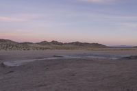 a large rock sitting on top of a field near a dry landscape under a pink sky