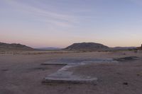 a large rock sitting on top of a field near a dry landscape under a pink sky