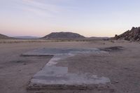 a large rock sitting on top of a field near a dry landscape under a pink sky