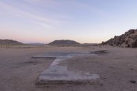 a large rock sitting on top of a field near a dry landscape under a pink sky