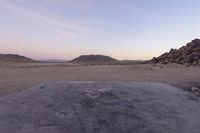 a large rock sitting on top of a field near a dry landscape under a pink sky
