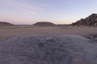 a large rock sitting on top of a field near a dry landscape under a pink sky